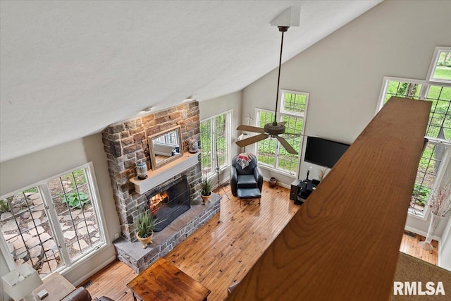 living room featuring a ceiling fan, vaulted ceiling, a textured ceiling, wood finished floors, and a fireplace