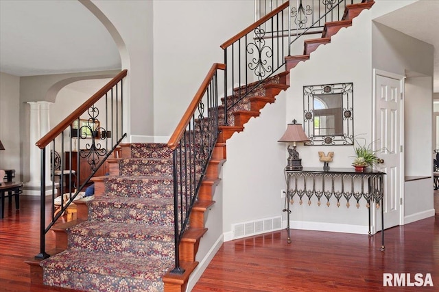 stairs featuring wood finished floors, a high ceiling, visible vents, baseboards, and arched walkways