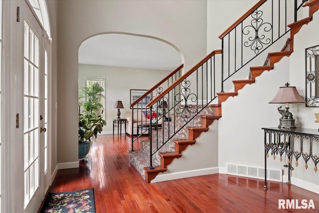 foyer with hardwood / wood-style floors, visible vents, baseboards, stairway, and arched walkways