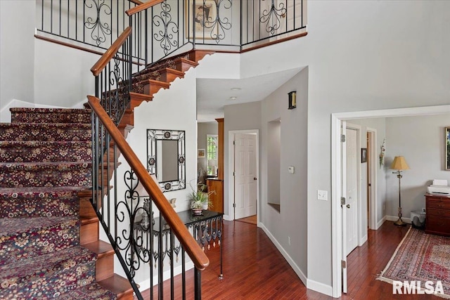 stairway featuring a towering ceiling, wood finished floors, and baseboards