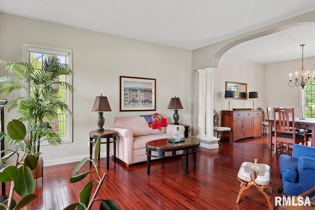 living room featuring an inviting chandelier, ornate columns, baseboards, arched walkways, and dark wood-style floors
