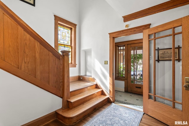 foyer entrance with stairway, baseboards, high vaulted ceiling, and wood finished floors