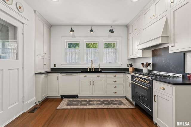 kitchen featuring a sink, dark wood finished floors, custom exhaust hood, gas range oven, and dark countertops