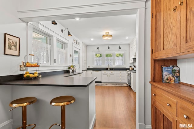 kitchen featuring high end stainless steel range oven, light wood finished floors, a sink, a kitchen bar, and dark countertops