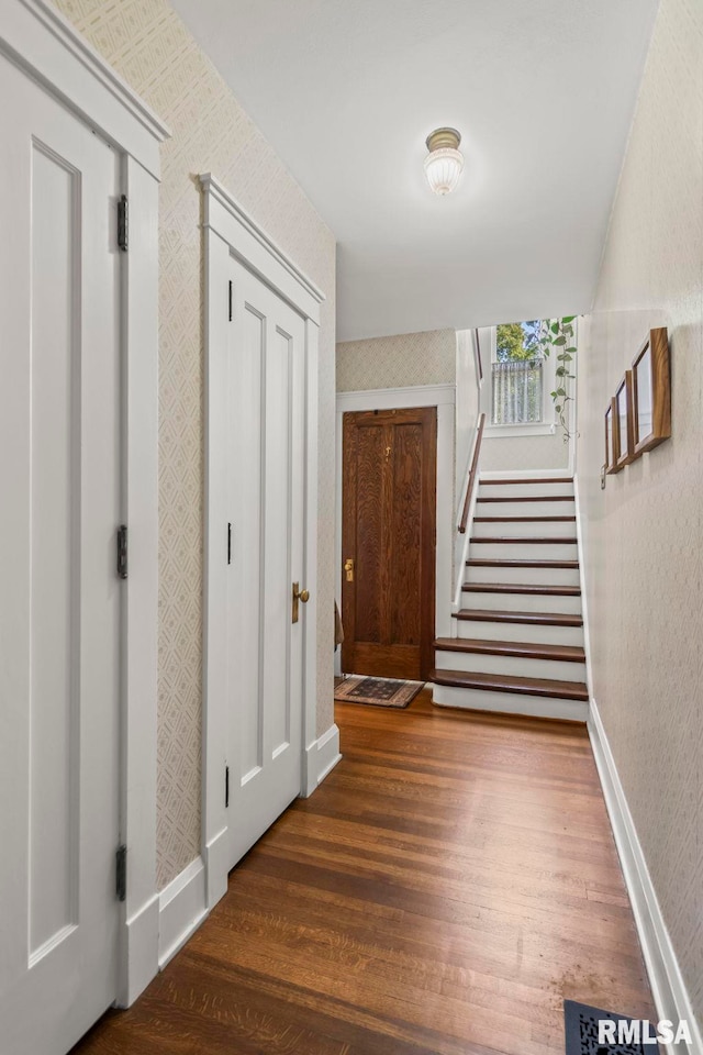 hallway featuring stairway, baseboards, wallpapered walls, and wood finished floors