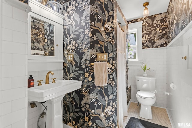 half bathroom with tile walls, wallpapered walls, toilet, wainscoting, and tile patterned floors