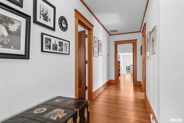 hallway featuring baseboards, ornamental molding, light wood-style flooring, and visible vents