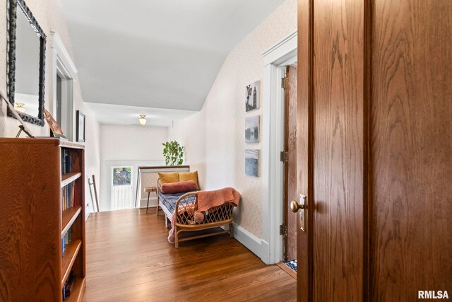 sitting room with baseboards, vaulted ceiling, wallpapered walls, and wood finished floors
