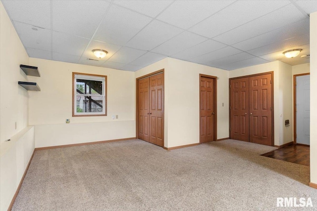 unfurnished bedroom featuring baseboards, a drop ceiling, and carpet flooring