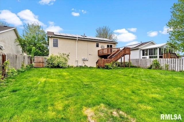 back of property with roof mounted solar panels, a deck, a lawn, and a fenced backyard