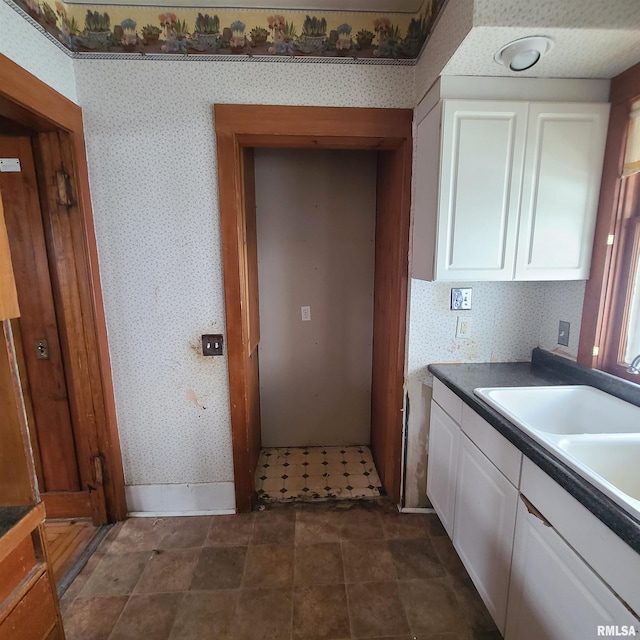 207 W Main St, Knoxville, IL 61448 - kitchen featuring wallpapered walls, baseboards, a sink, white cabinetry, and dark countertops