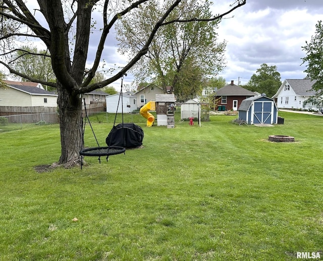 view of yard with an outbuilding, fence, a fire pit, a playground, and a storage unit