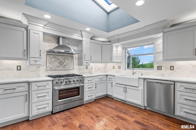 kitchen with a sink, a skylight, stainless steel appliances, tasteful backsplash, and wall chimney range hood