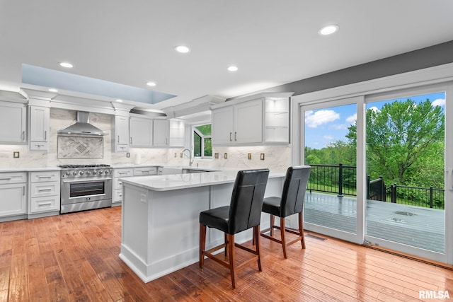 kitchen with a peninsula, a breakfast bar, high end stainless steel range oven, backsplash, and wall chimney range hood