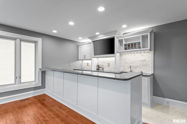 kitchen featuring baseboards, visible vents, dark stone counters, a peninsula, and tasteful backsplash