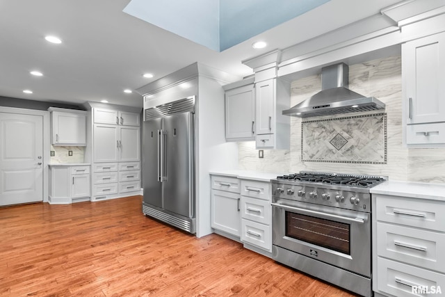 kitchen featuring tasteful backsplash, recessed lighting, wall chimney exhaust hood, light countertops, and high end appliances