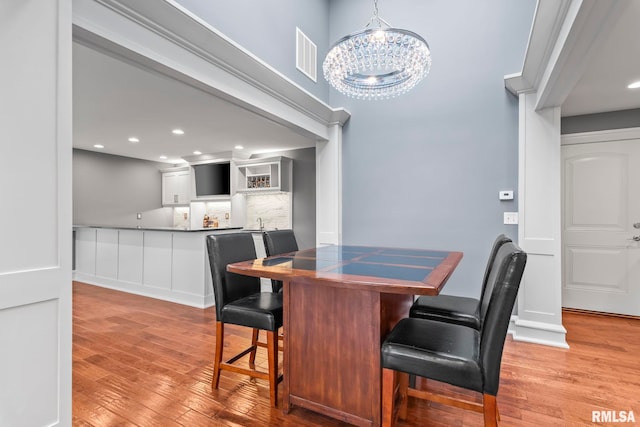 dining room with light wood-type flooring, visible vents, bar area, and a notable chandelier