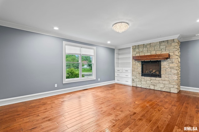 unfurnished living room with wood finished floors, baseboards, a stone fireplace, ornamental molding, and recessed lighting