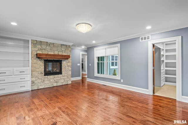 unfurnished living room featuring wood finished floors, ornamental molding, visible vents, baseboards, and a stone fireplace
