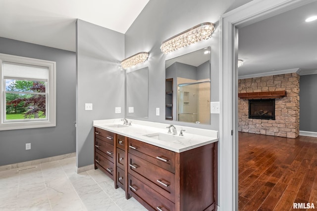 bathroom featuring baseboards, a shower stall, a stone fireplace, and a sink