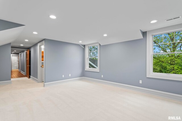 spare room featuring light colored carpet, a wealth of natural light, baseboards, and visible vents