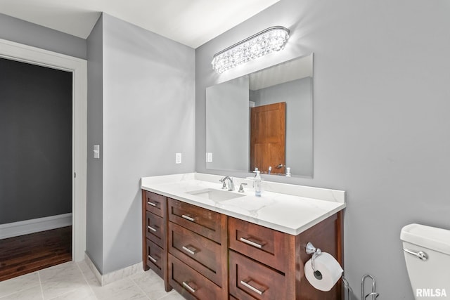 half bathroom with baseboards, marble finish floor, vanity, and toilet