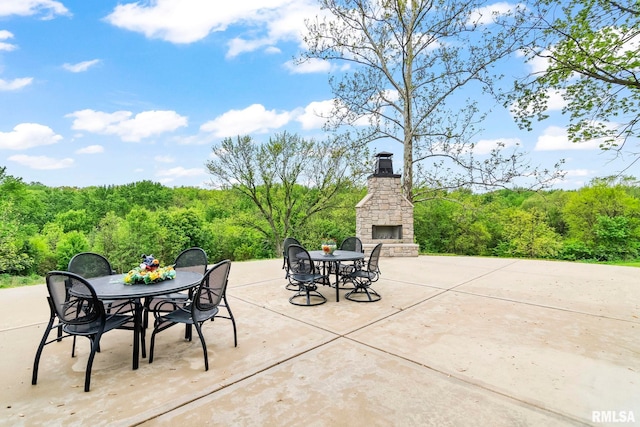 view of patio featuring an outdoor stone fireplace, outdoor dining space, and a forest view