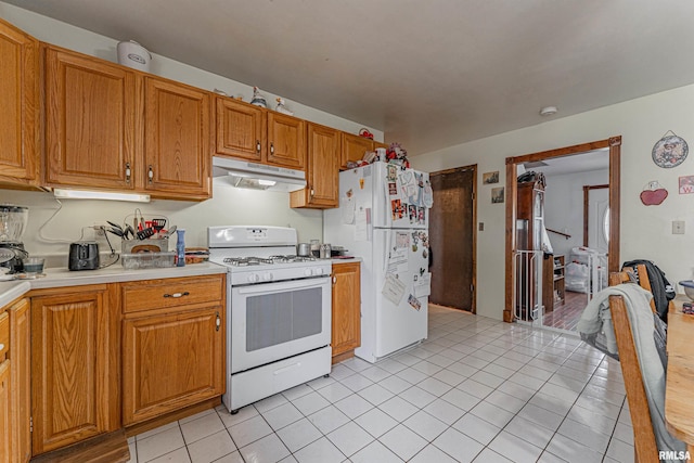 kitchen with brown cabinetry, white appliances, under cabinet range hood, light countertops, and light tile patterned floors