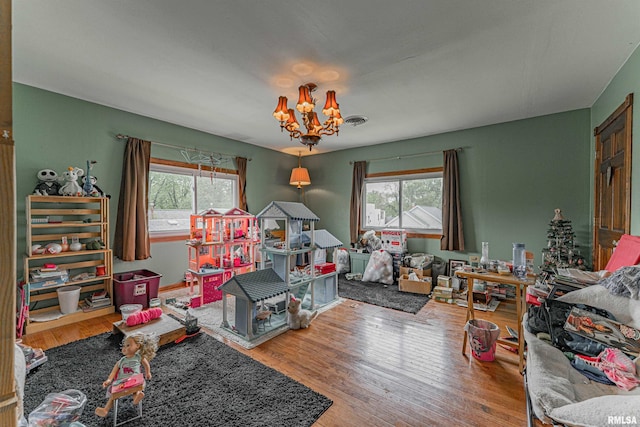 rec room with an inviting chandelier, visible vents, a healthy amount of sunlight, and wood finished floors