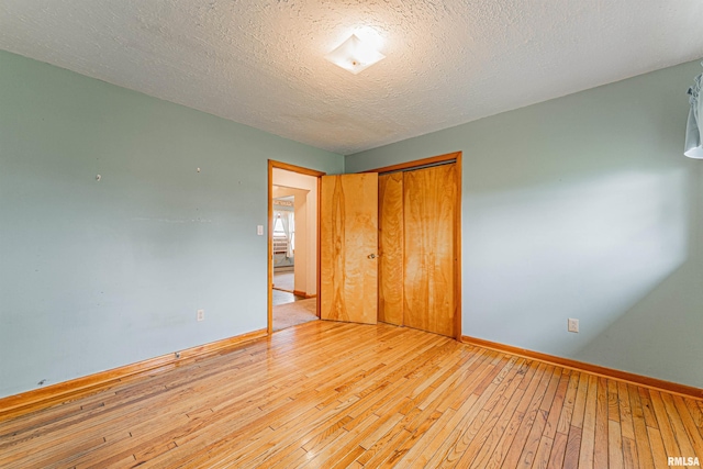 unfurnished bedroom featuring baseboards, a closet, light wood-style flooring, and a textured ceiling