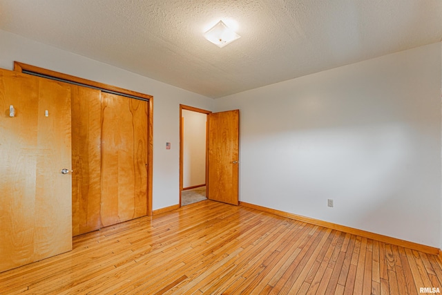 unfurnished bedroom with baseboards, light wood-style floors, a closet, and a textured ceiling