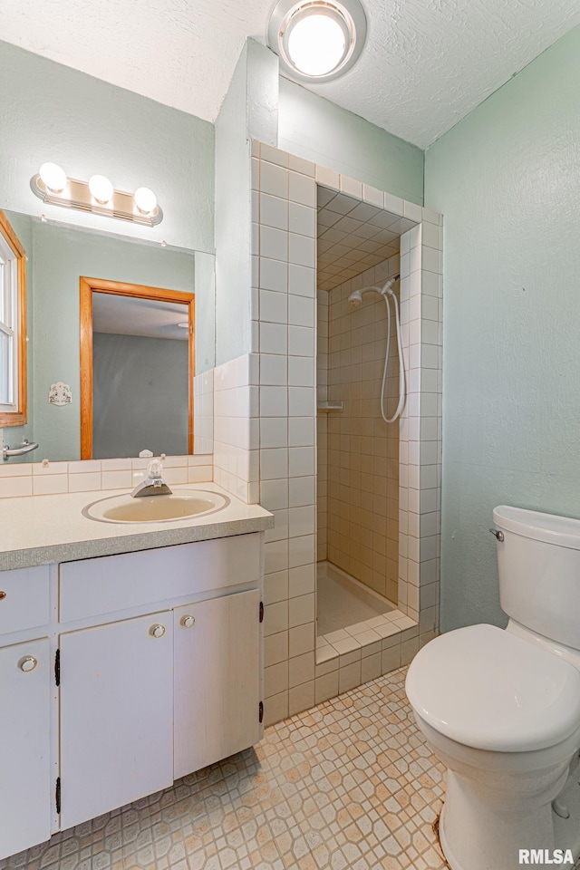 full bathroom with vanity, toilet, a tile shower, and a textured ceiling