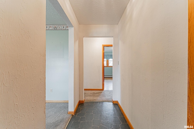 hall with baseboards, stone finish flooring, and a textured ceiling