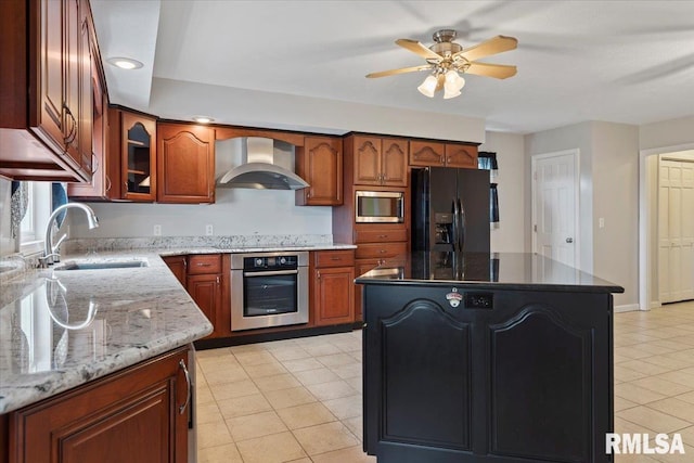 kitchen featuring a sink, wall chimney range hood, black appliances, ceiling fan, and light stone countertops