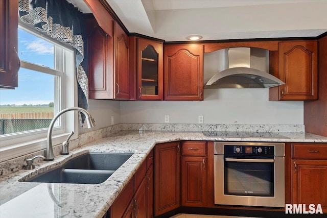 kitchen with a sink, wall chimney range hood, black electric stovetop, oven, and light stone counters