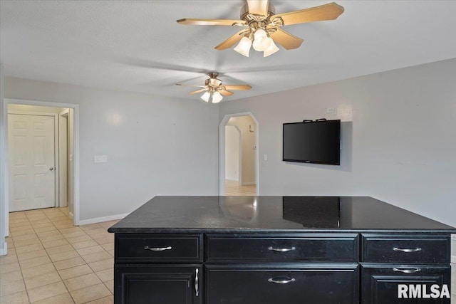 interior space with a ceiling fan, baseboards, dark cabinets, and light tile patterned flooring