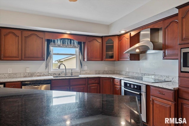 kitchen featuring a sink, stainless steel appliances, dark stone counters, wall chimney exhaust hood, and glass insert cabinets