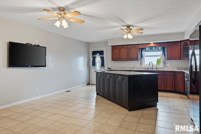 kitchen featuring a ceiling fan, freestanding refrigerator, a center island, baseboards, and a sink