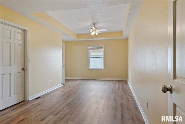 unfurnished room with a tray ceiling, light wood-style flooring, baseboards, and ceiling fan