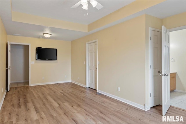 unfurnished living room featuring a ceiling fan, a raised ceiling, baseboards, and light wood-type flooring