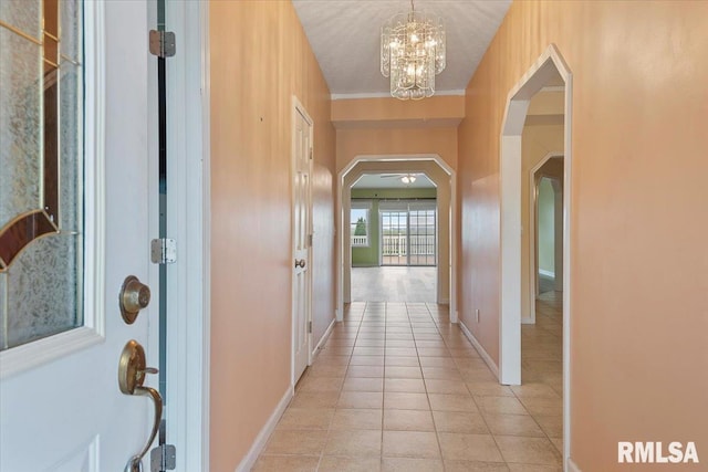hall with arched walkways, baseboards, an inviting chandelier, and light tile patterned flooring