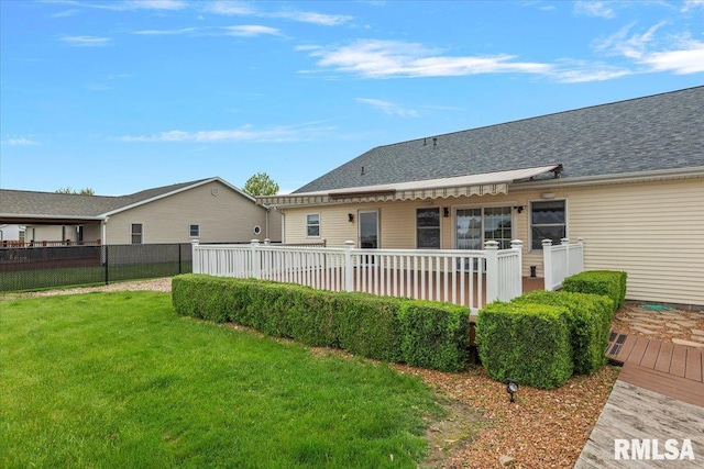 rear view of property featuring a lawn, a wooden deck, a shingled roof, and fence