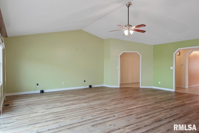 interior space with wood finished floors, a ceiling fan, baseboards, arched walkways, and vaulted ceiling