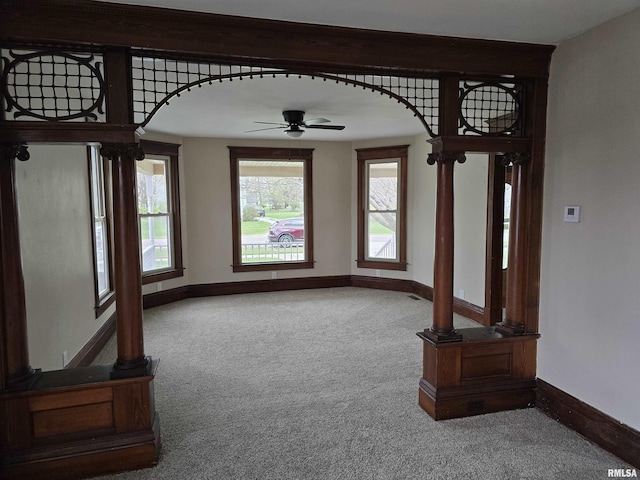 unfurnished dining area featuring arched walkways, baseboards, ceiling fan, and carpet floors