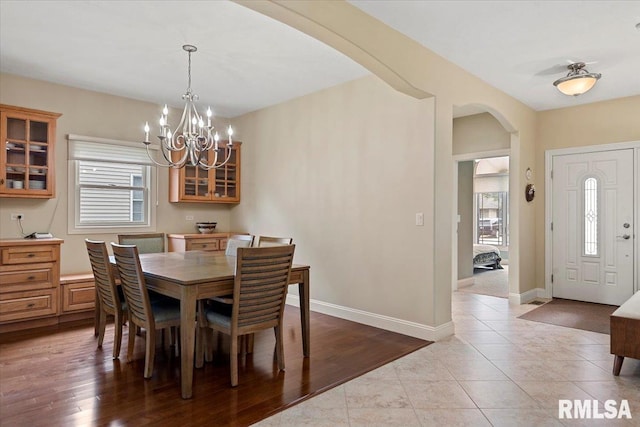 tiled dining area with plenty of natural light, baseboards, arched walkways, and a notable chandelier
