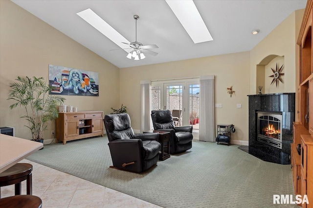 living area featuring a fireplace, a skylight, baseboards, ceiling fan, and light carpet