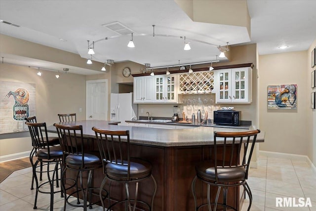 kitchen with white fridge with ice dispenser, visible vents, baseboards, a kitchen island, and black microwave