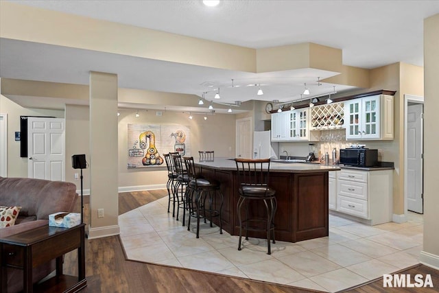 kitchen with a center island, glass insert cabinets, white refrigerator with ice dispenser, black microwave, and a kitchen breakfast bar