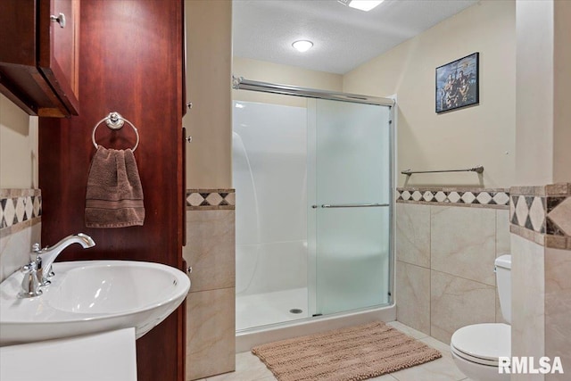 bathroom featuring tile walls, a textured ceiling, toilet, wainscoting, and a shower stall