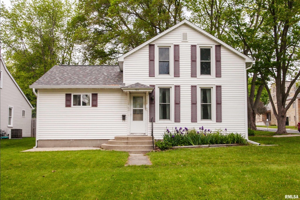 traditional-style house featuring a front lawn, a shingled roof, entry steps, and central AC unit